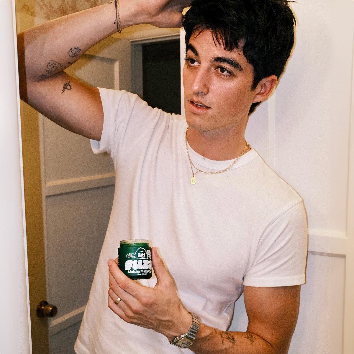 Person holding a can of FUZZ Matcha Matte Clay while looking in a mirror
